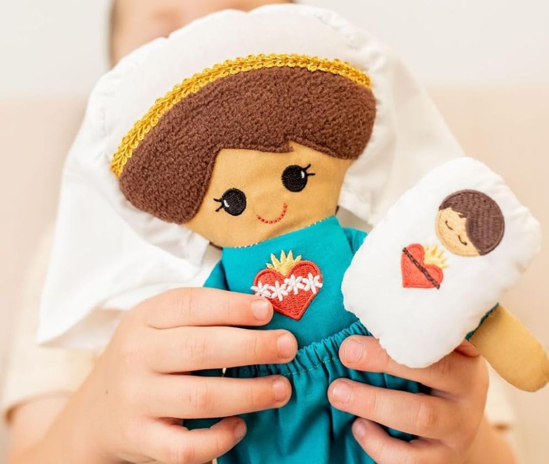 Child holding a handmade doll and pillow, both embroidered with heart motifs.